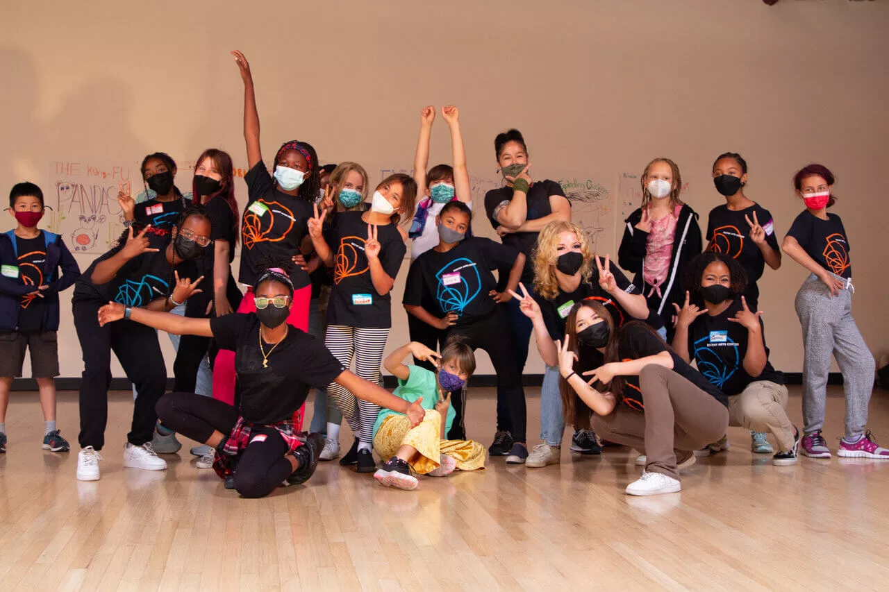A Group of racially diverse Camp Destiny youth ages 5-13, counselors, and teaching artists posing for a fun group photo in the dance studio